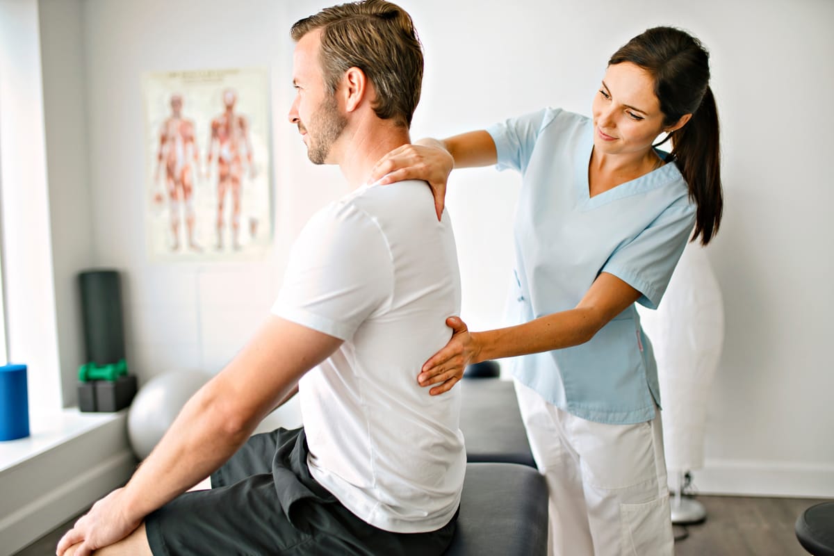 Female chiropractor examining a male patient's back in a clinical setting