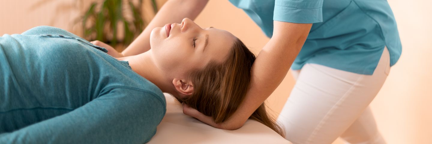 Woman with a peaceful expression receiving a gentle neck adjustment from a chiropractor in warm, comfortable lighting